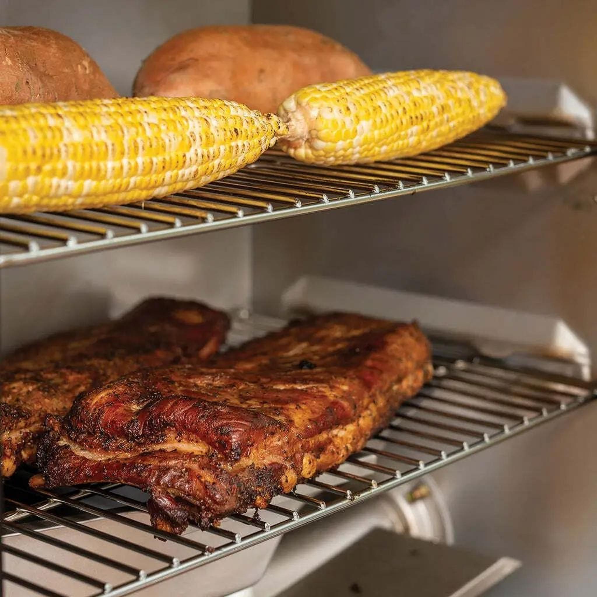 Ribs, corn and sweet potatoes cooking on smoker racks